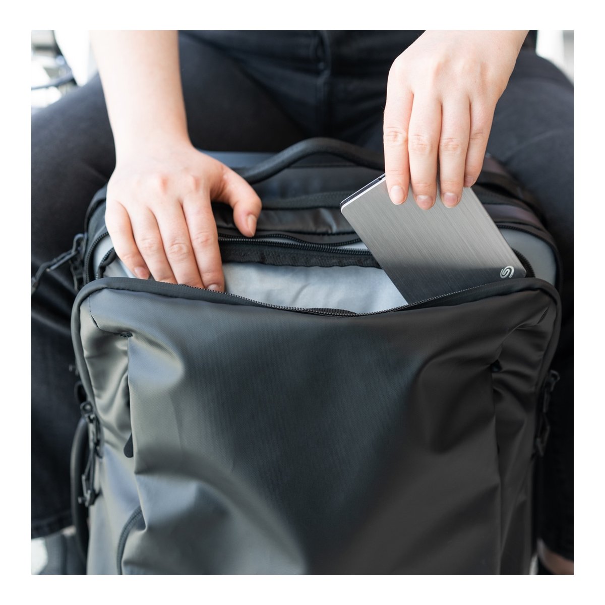 WANDRD Transit Carry-On Roller - Anwendungsbeispiel: Person verstaut externe Festplatte in Rucksackfach