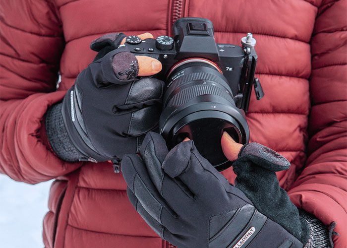Person trägt Winterhandschuhe mit freigelegten Fingerspitzen und stellt das Objektiv einer Kamera ein.
