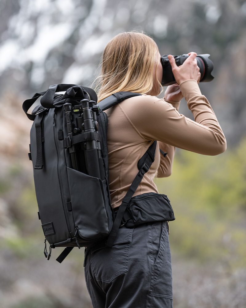 Frau fotografiert in der Natur mit einem schwarzen Wandrd PRVKE V4 Rucksack und Stativ