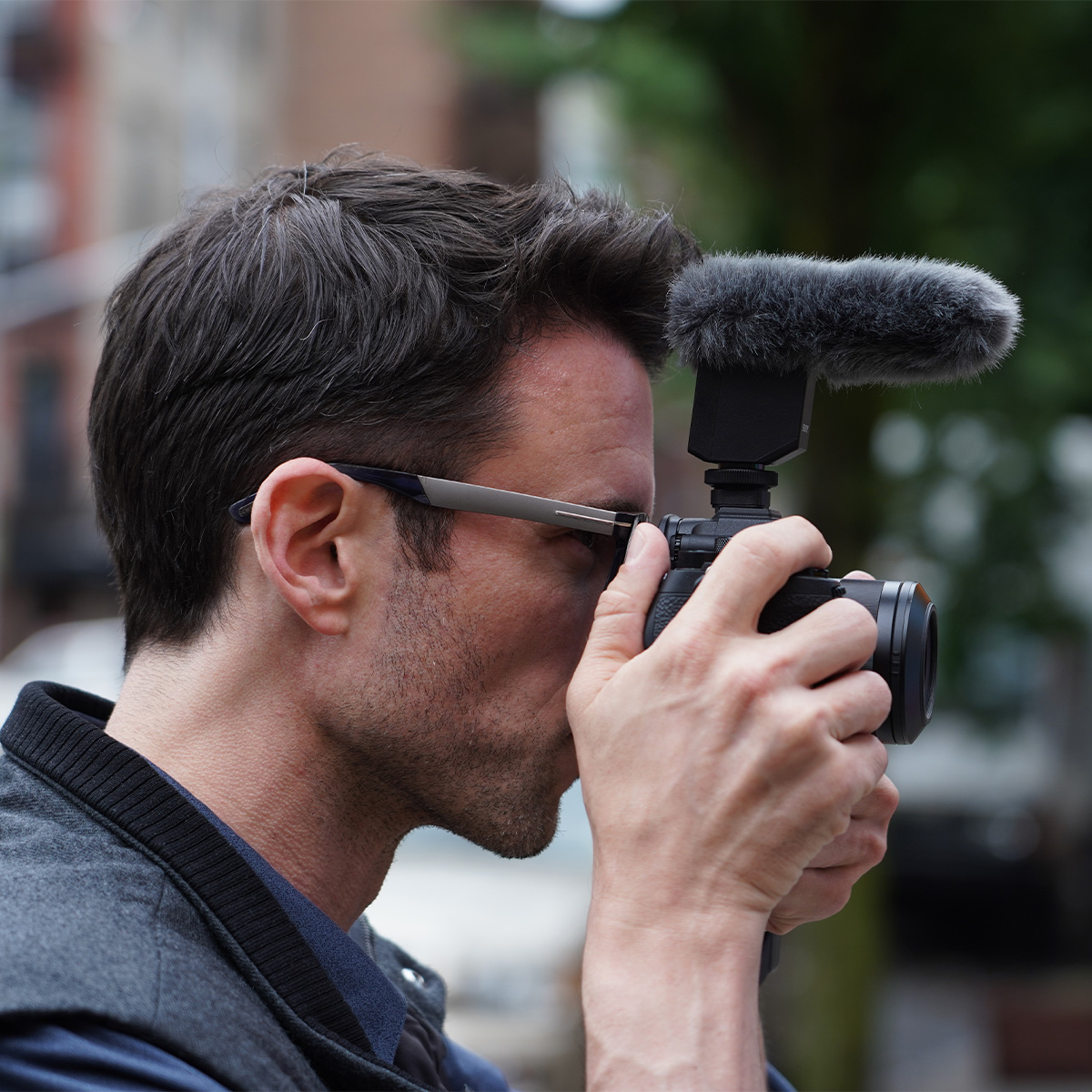 Nahaufnahme von dem Kopf eines Mannes, der eine Sony Alpha Kamera mit dem  Sony ECM-B1M Mikrofon vor seine Augen hält
