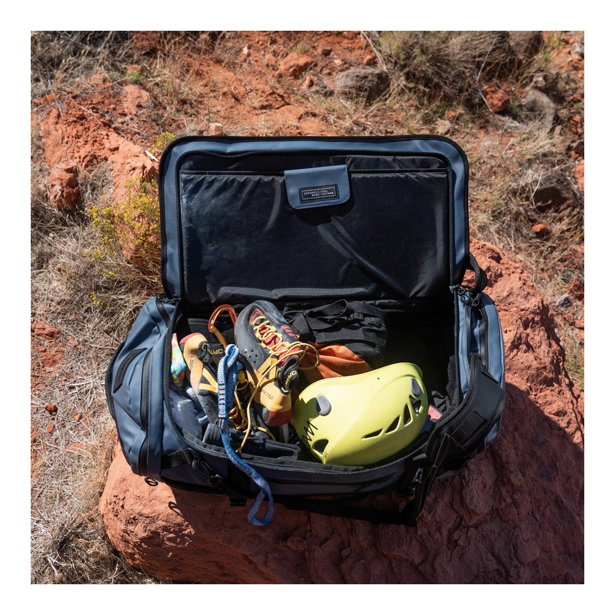 WANDRD HEXAD CARRYALL DUFFEL 40-Liter Aegean Blue - Anwendungsbeispiel: Offener Duffel Bag mit Kletterausrüstung (Schuhe, Helm, Seil) auf Fels. WANDRD HEXAD CARRYALL DUFFEL 40-Liter Aegean Blue - Anwendungsbeispiel: Offener Duffel Bag mit Kletterausrüstung (Schuhe, Helm, Seil) auf Fels.