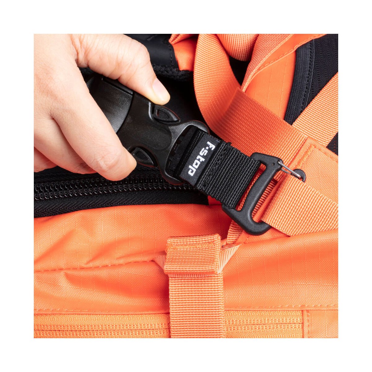 F-Stop Navin Anthrazit (geschweisst) - DETAILANSICHT: HAND ÖFFNET SCHNALLE MIT F-STOP LOGO AM ORANGEFARBENEN RUCKSACK. F-Stop Navin Anthrazit (geschweisst) - DETAILANSICHT: HAND ÖFFNET SCHNALLE MIT F-STOP LOGO AM ORANGEFARBENEN RUCKSACK.