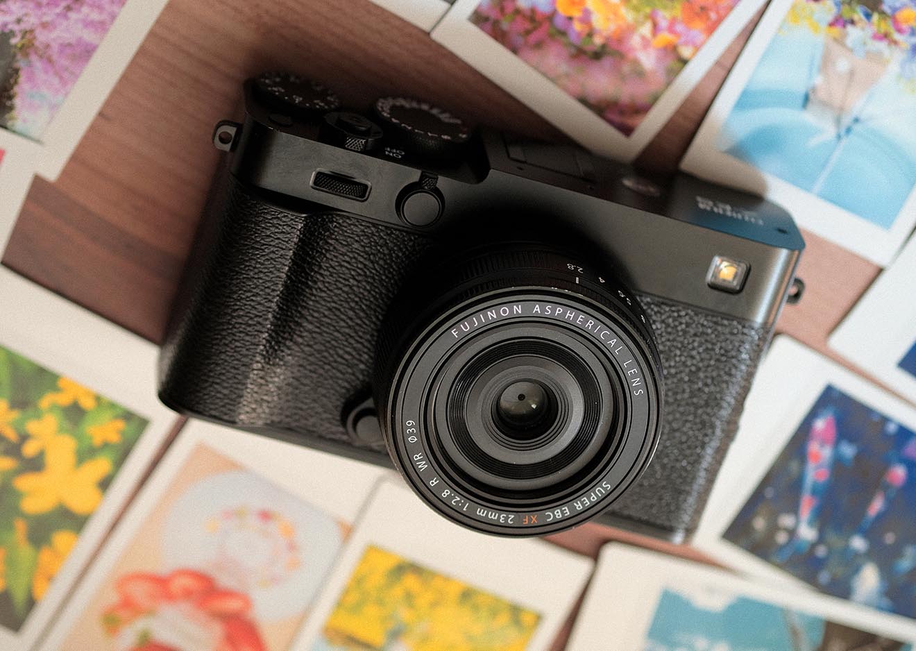 Fujifilm X-E5 in Schwarz mit 23mm Pancake-Objektiv, liegend zwischen ausgedruckten Bildern – ideal für kreative Fotografie