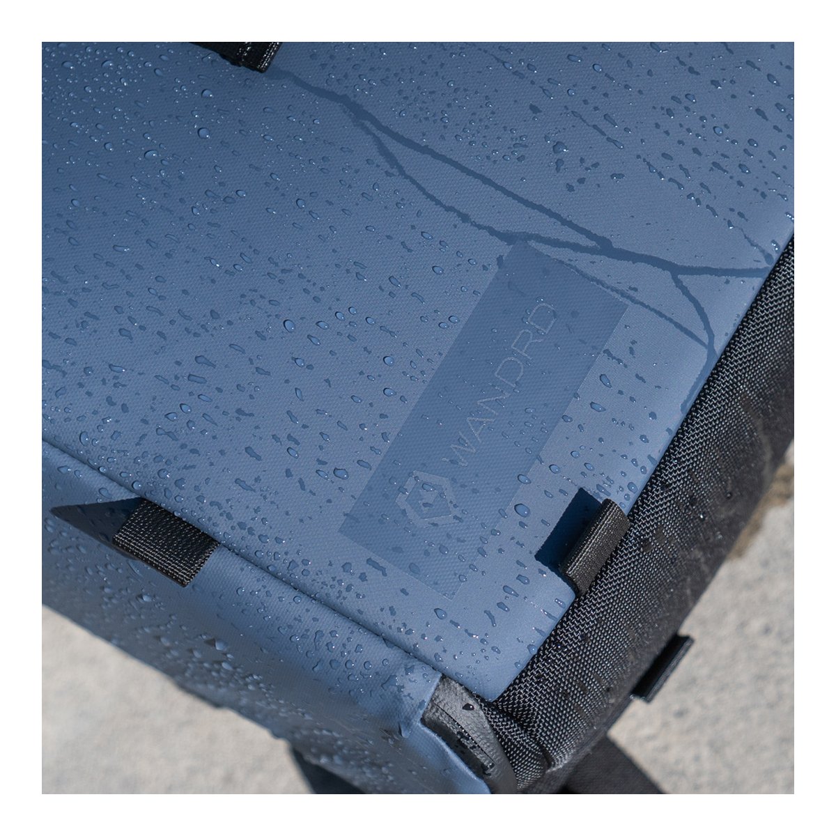 WANDRD PRVKE Lite 11-Liter Blue - Detailansicht: Wasserdichte Oberfläche des blauen Rucksacks mit Wassertropfen und Wandrd-Logo. WANDRD PRVKE Lite 11-Liter Blue - Detailansicht: Wasserdichte Oberfläche des blauen Rucksacks mit Wassertropfen und Wandrd-Logo.