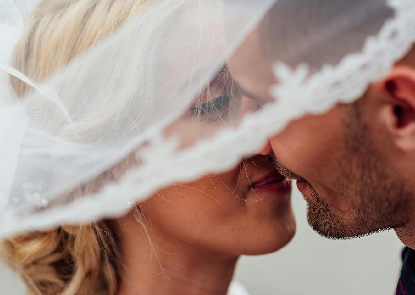 Intimer Kussmoment unter dem Brautschleier Braut und Bräutigam küssen sich unter dem Schleier – romantisches Hochzeitsfoto