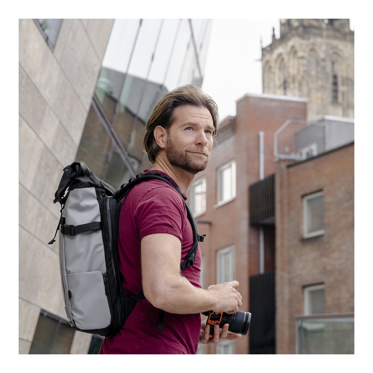WANDRD PRVKE 31-Liter DisNet Grey Photo Bundle - Seitenansicht des Rucksacks an Mann mit Kamera in Stadt.