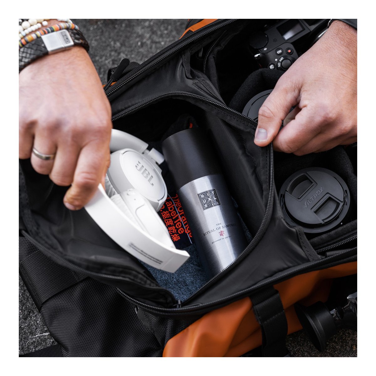WANDRD PRVKE 21-Liter Sedona Orange Photo Bundle V3 - Anwendungsbeispiel: Innenansicht der geöffneten Tasche mit verstauten Kopfhörern, Spray und Kameraausrüstung.