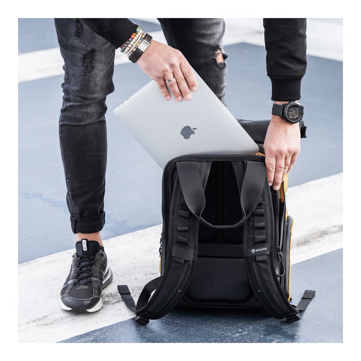 WANDRD PRVKE Lite 11-Liter Dallol Yellow - Anwendungsbeispiel: Person verstaut Laptop in Rucksack-Laptopfach; Rückansicht mit Gurten.