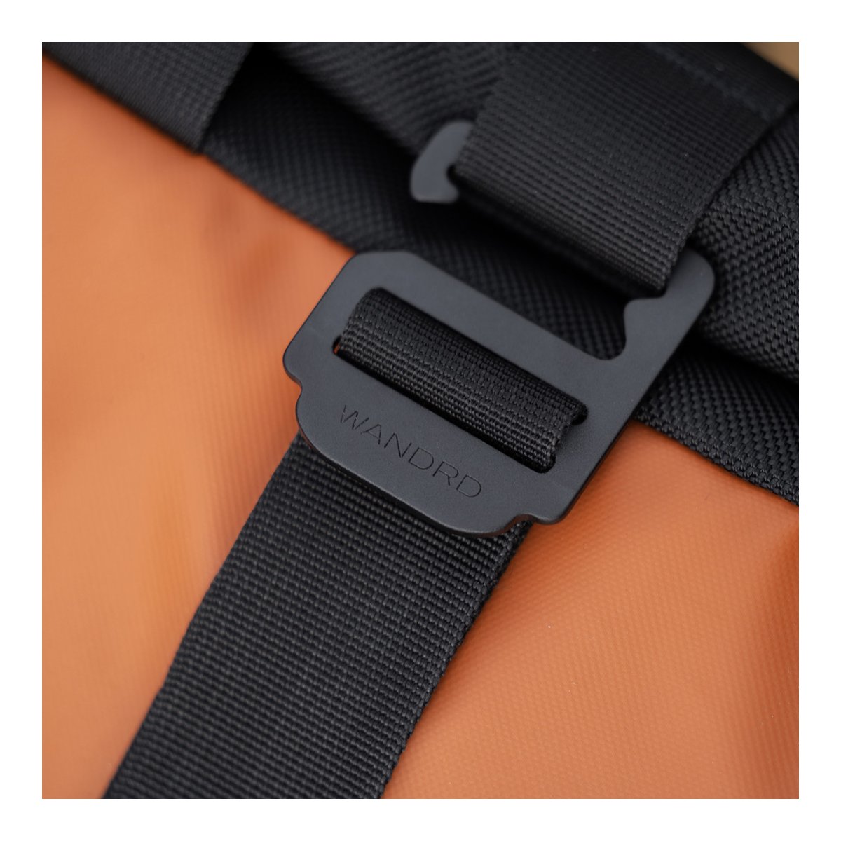 WANDRD PRVKE Lite 11-Liter Sedona Orange - Detailansicht der schwarzen WANDRD-Schnalle und des Gurts auf orangefarbenem Material