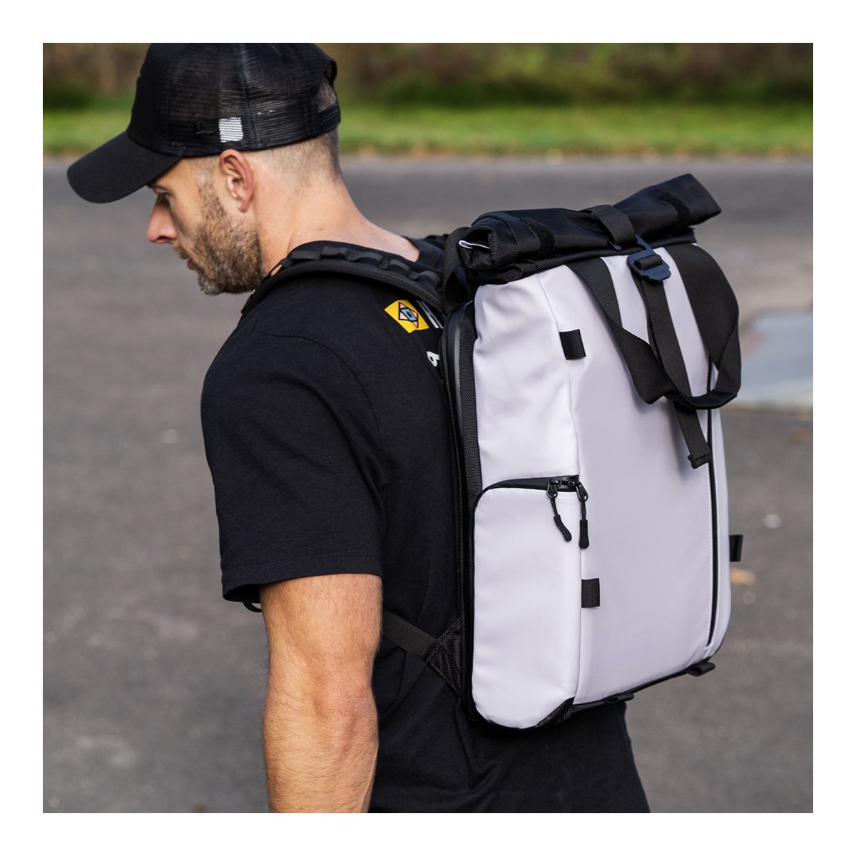 WANDRD PRVKE Lite 11-Liter Uyuni Purple - Anwendungsbeispiel: Mann trägt den hellgrauen Roll-Top-Rucksack seitlich, Reißverschlusstasche sichtbar.