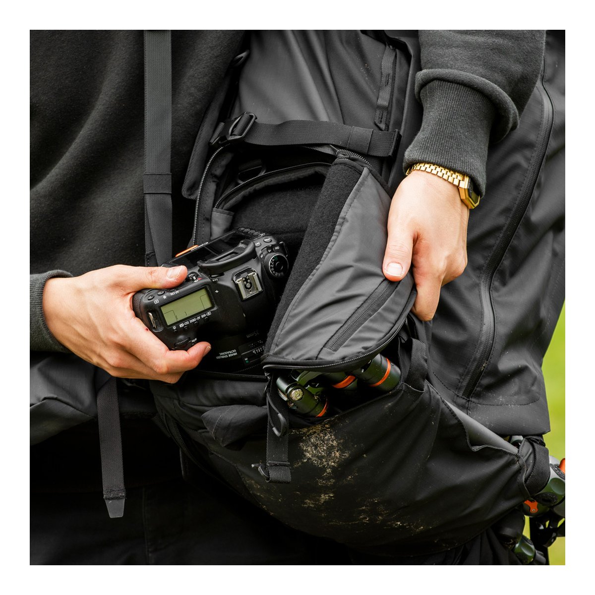 Wandrd Fernweh 50L S/M Schwarz - Anwendungsbeispiel: Person verstaut Kamera in Rucksackfach; Stativbein sichtbar.