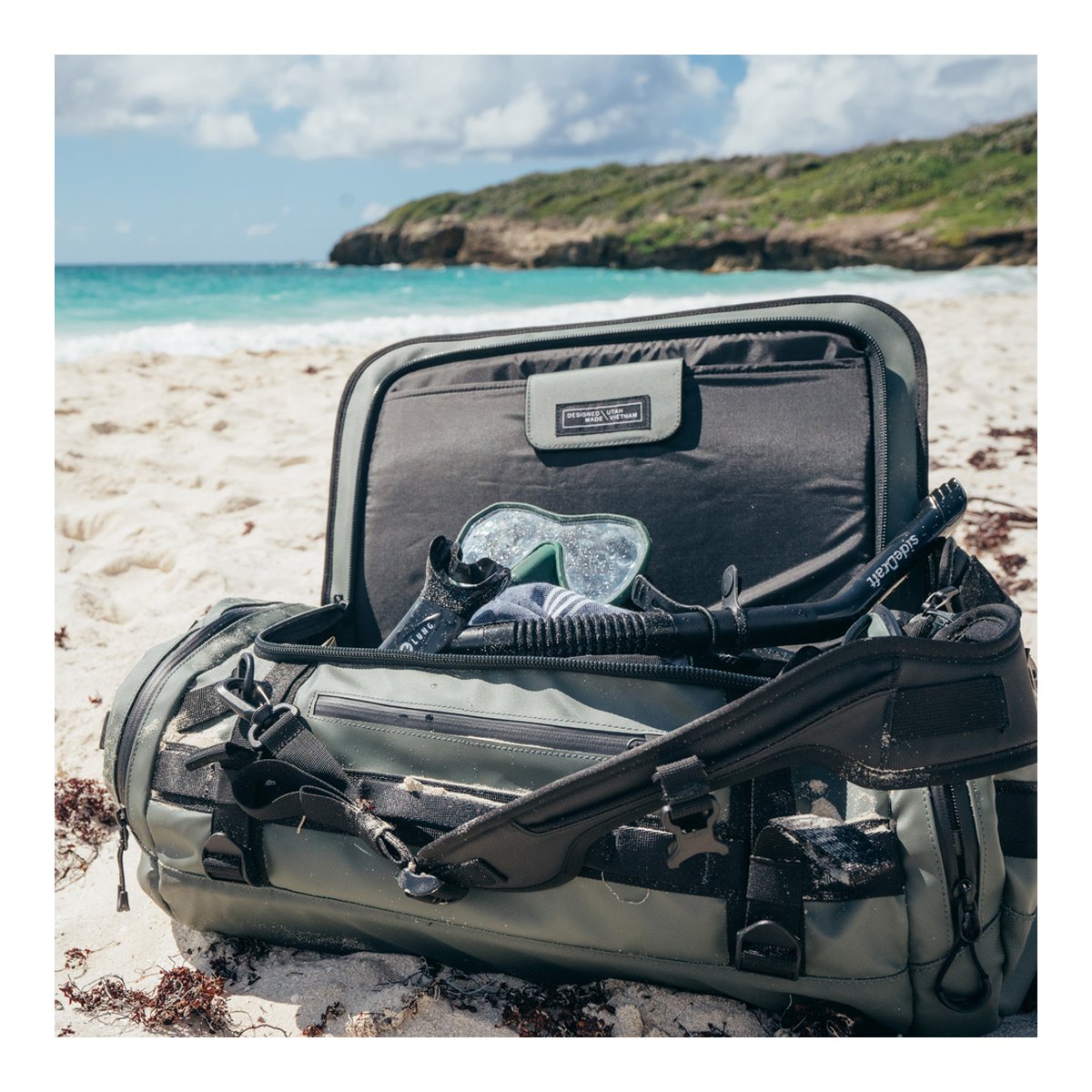 WANDRD HEXAD CARRYALL DUFFEL 40-Liter Wasatch Green - Anwendungsbeispiel: Reisetasche offen am Strand, gefüllt mit Schnorchel-Set