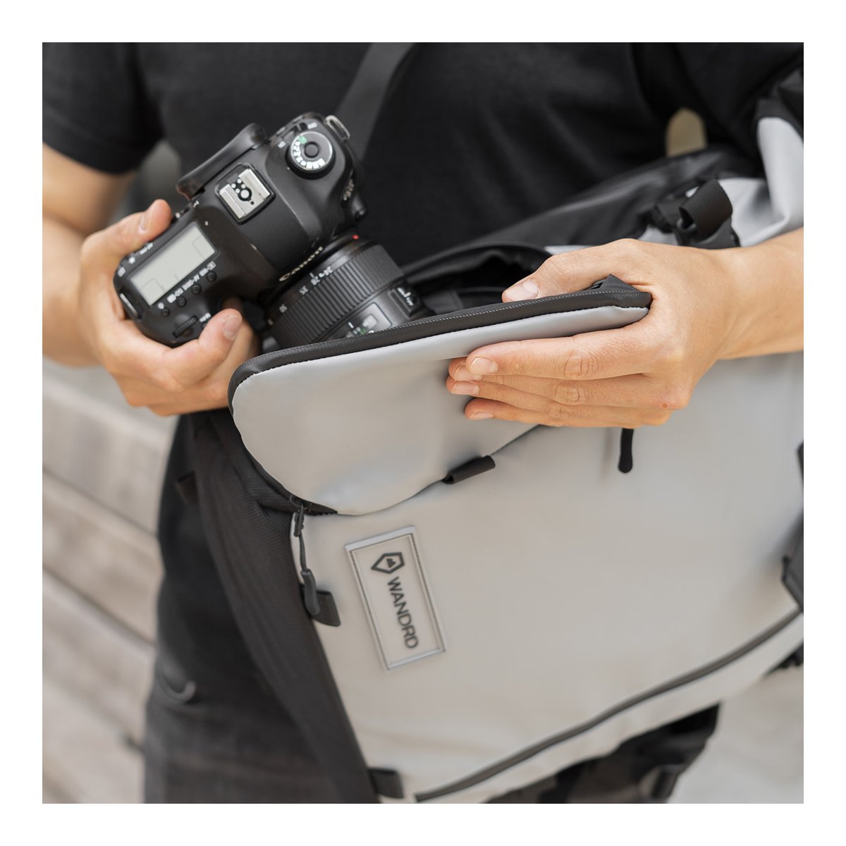 WANDRD PRVKE 21-Liter DisNet Grey Photo Bundel V3 - Anwendungsbeispiel: Person verstaut Kamera in grauer Wandrd Umhängetasche. WANDRD PRVKE 21-Liter DisNet Grey Photo Bundel V3 - Anwendungsbeispiel: Person verstaut Kamera in grauer Wandrd Umhängetasche.