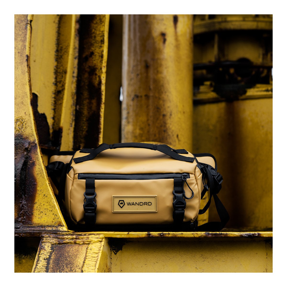 WANDRD ROGUE Sling 6L Dallol Yellow - Beige Wandrd-Hüfttasche, Frontansicht, auf gelbem, industriellem Hintergrund.