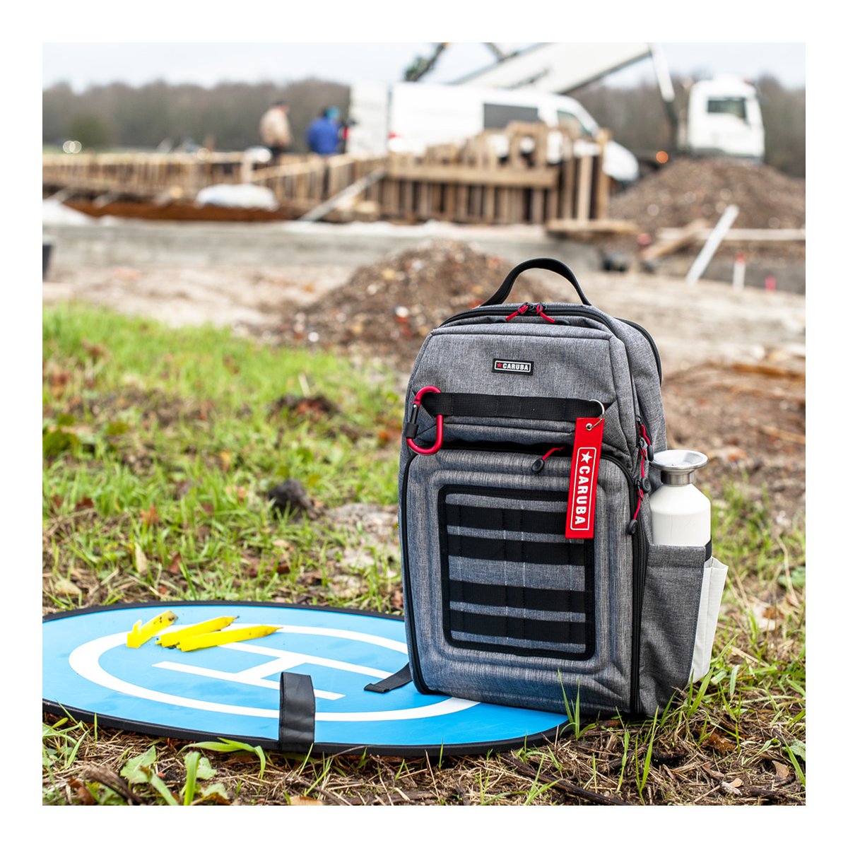 Caruba Skyline 100 Drohnenpack Grau - Anwendungsbeispiel: Grauer Rucksack mit Wasserflasche und Drohnenlandeplatz im Freien.