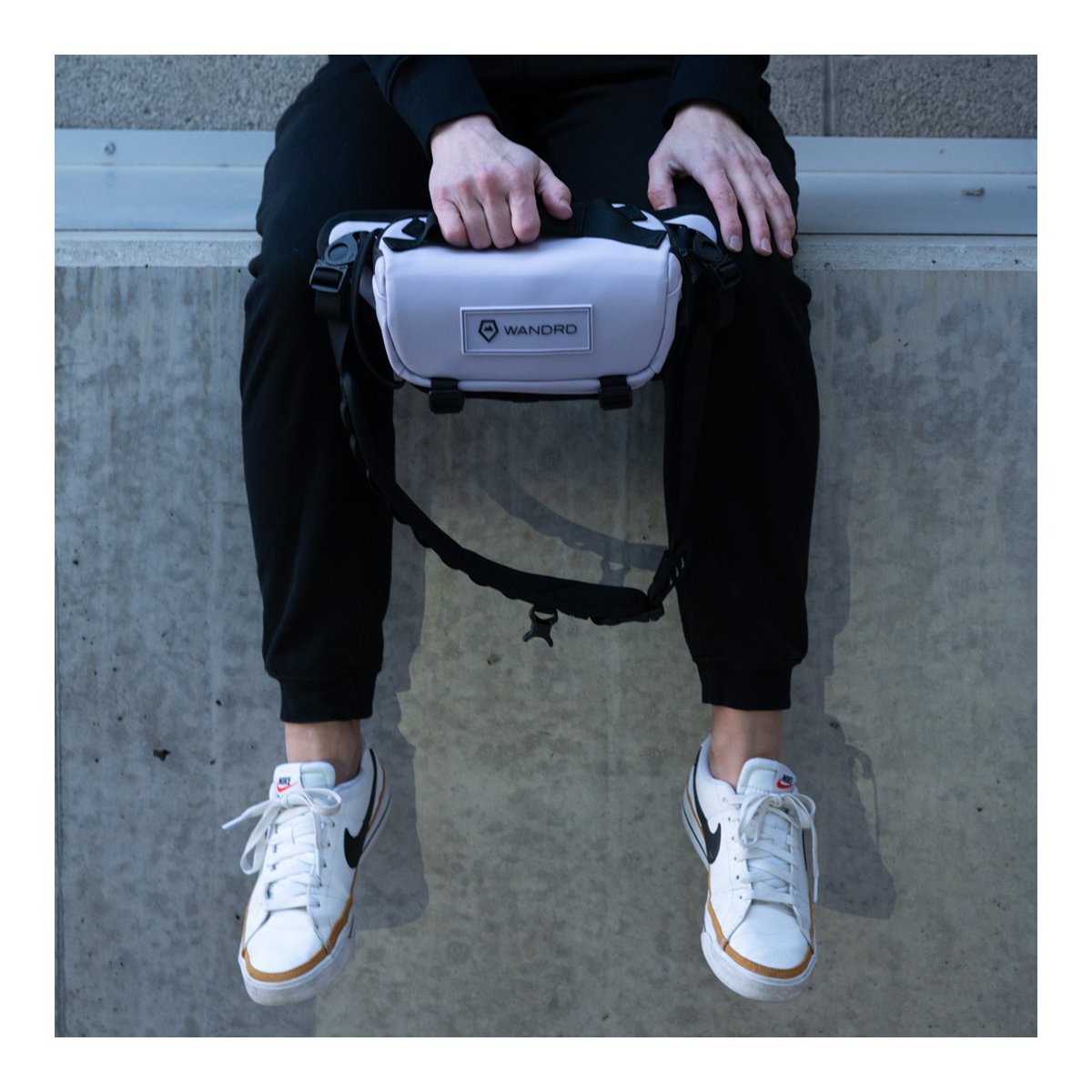 WANDRD ROGUE Sling 3L Uyuni Purple - Anwendungsbeispiel: Helle Tasche zwischen den Händen einer sitzenden Person. WANDRD ROGUE Sling 3L Uyuni Purple - Anwendungsbeispiel: Helle Tasche zwischen den Händen einer sitzenden Person.