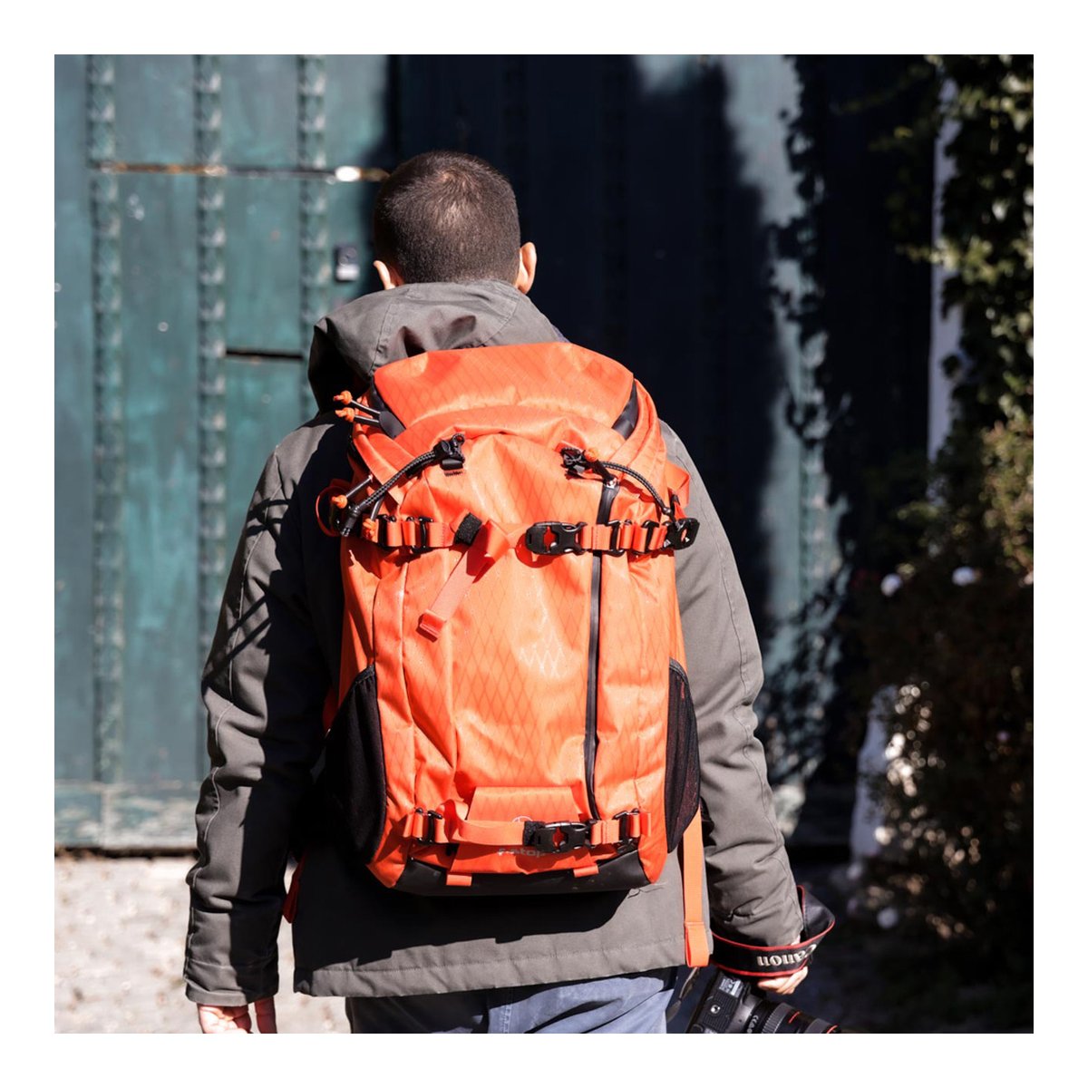 F-Stop DuraDiamond Ajna - Magma - Anwendungsbeispiel: Rückansicht des orangefarbenen Rucksacks am Rücken einer Person mit Kamera.