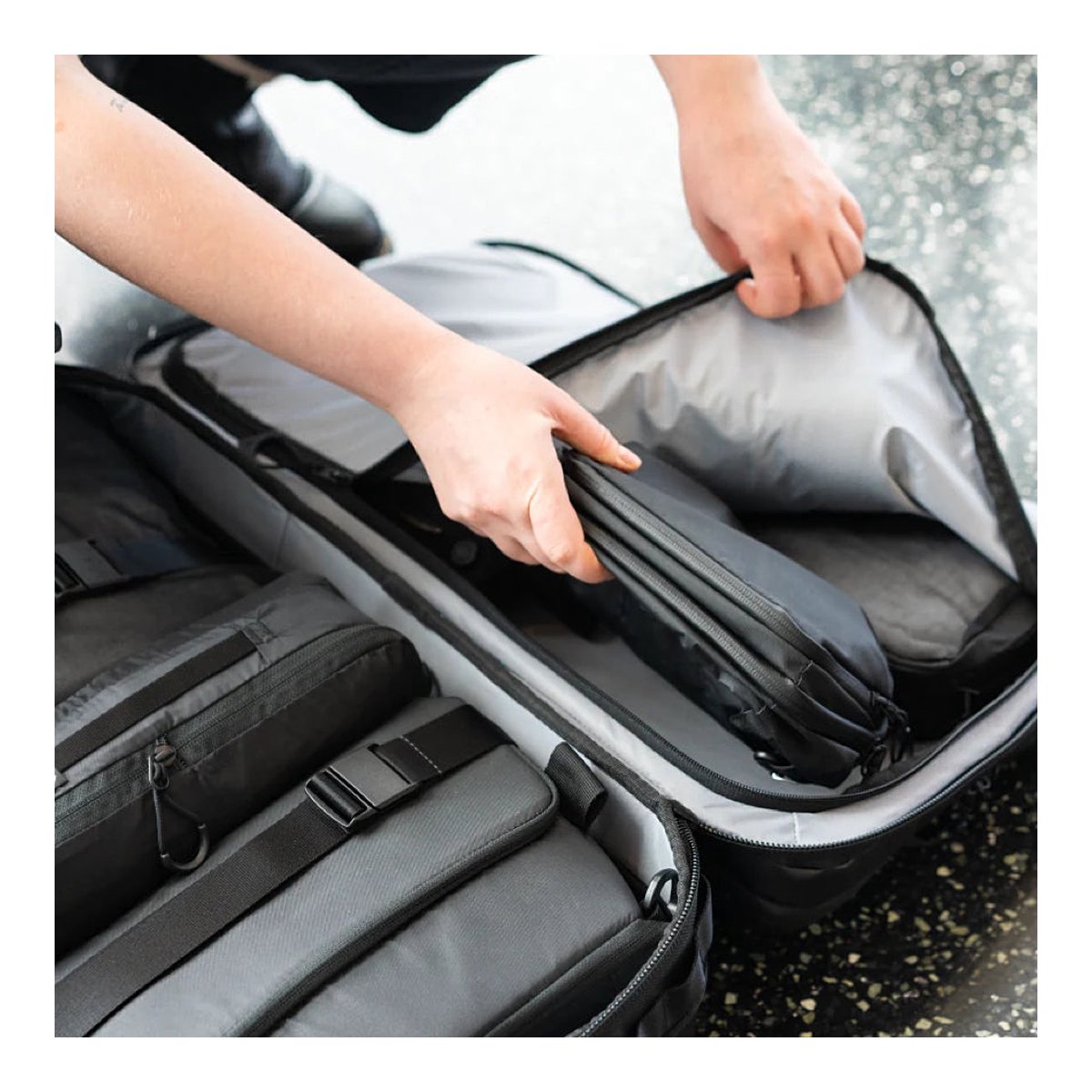 WANDRD Transit Carry-On Roller - Anwendungsbeispiel: Hände verstauen schwarze Organizer in offenem Koffer.
