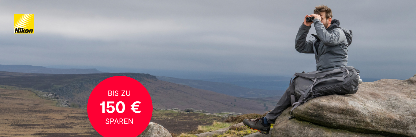 Nikon Cashback Aktion – Bis zu 150 € sparen Nikon Cashback Aktion – Outdoor Fotograf mit Fernglas auf Felsen, bis zu 150 Euro sparen