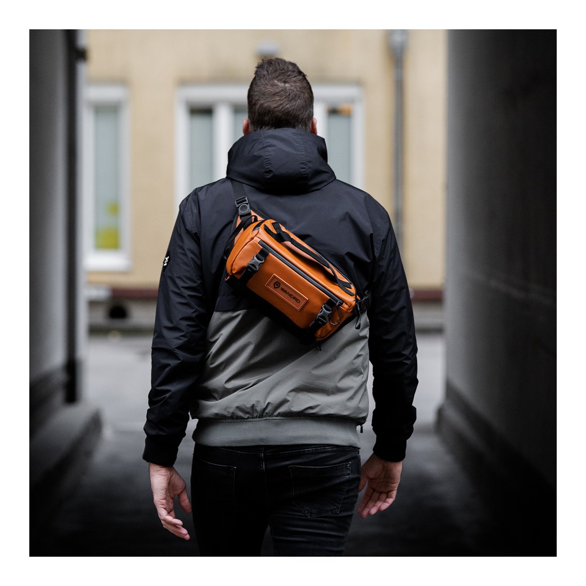 WANDRD ROGUE Sling 6L Sedona Orange - Anwendungsbeispiel (Rückansicht): Braune Umhängetasche wird von einem Mann auf dem Rücken getragen.