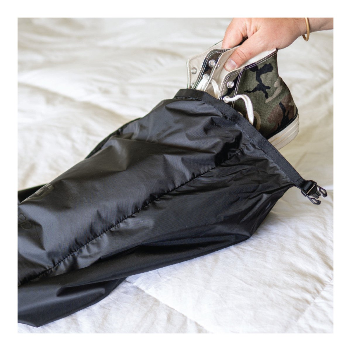 WANDRD Shoe Pouch - Anwendungsbeispiel: Ein Camouflage-Sneaker wird in den schwarzen Schuhbeutel gelegt.