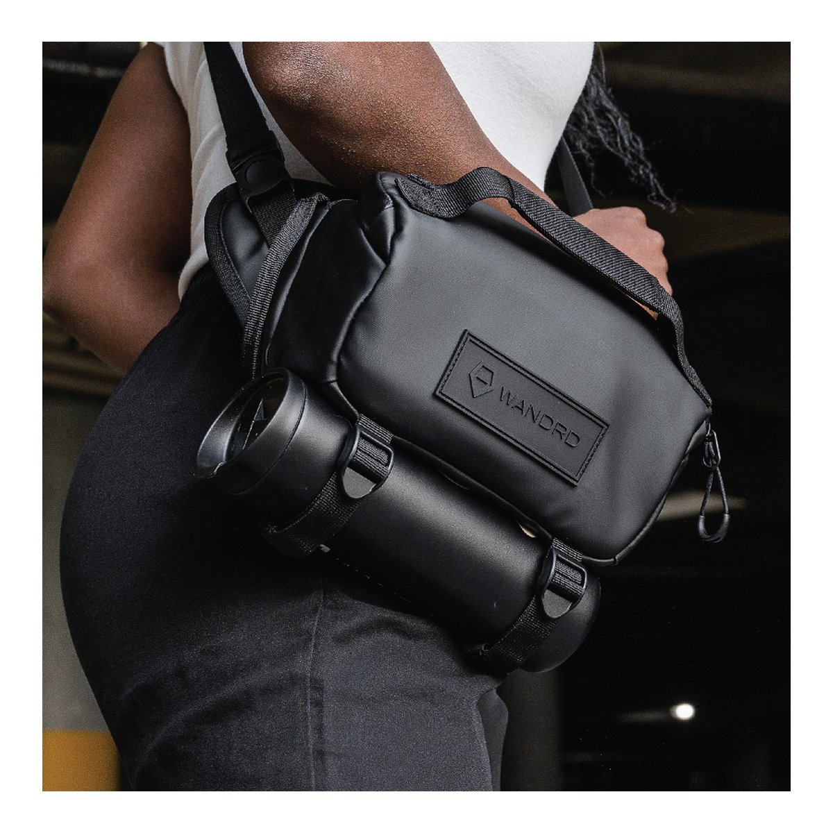 WANDRD ROGUE Sling 3L Black - Anwendungsbeispiel: Schwarze WANDRD-Tasche mit seitlich befestigter Trinkflasche, von Person getragen.