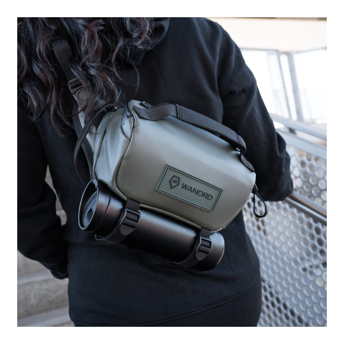 WANDRD ROGUE Sling 3L Wasatch Green - Anwendungsbeispiel: Grüne Sling Bag mit Trinkflasche, diagonal über Schulter getragen, Rückansicht.