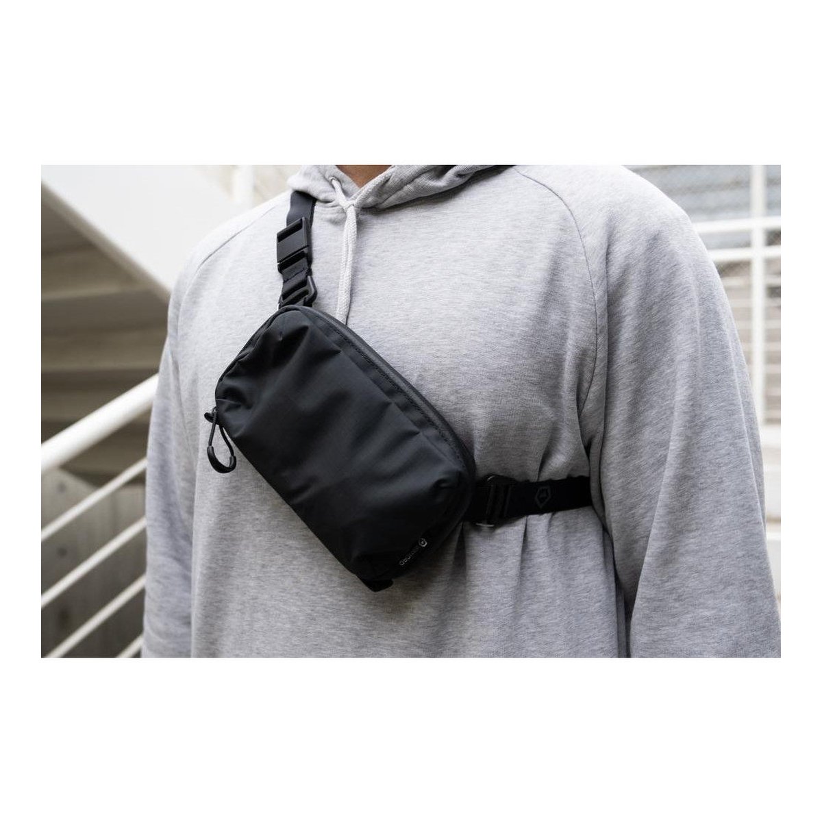 WANDRD Tech Bag Strap - Anwendungsbeispiel: Schwarze Sling Bag diagonal über grauem Hoodie getragen.