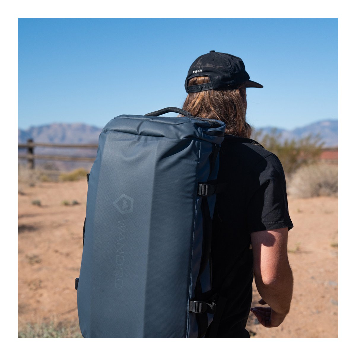 WANDRD HEXAD CARRYALL DUFFEL 40-Liter Aegean Blue - Rückansicht: Blauer WANDRD Rucksack wird von einer Person im Freien getragen. WANDRD HEXAD CARRYALL DUFFEL 40-Liter Aegean Blue - Rückansicht: Blauer WANDRD Rucksack wird von einer Person im Freien getragen.