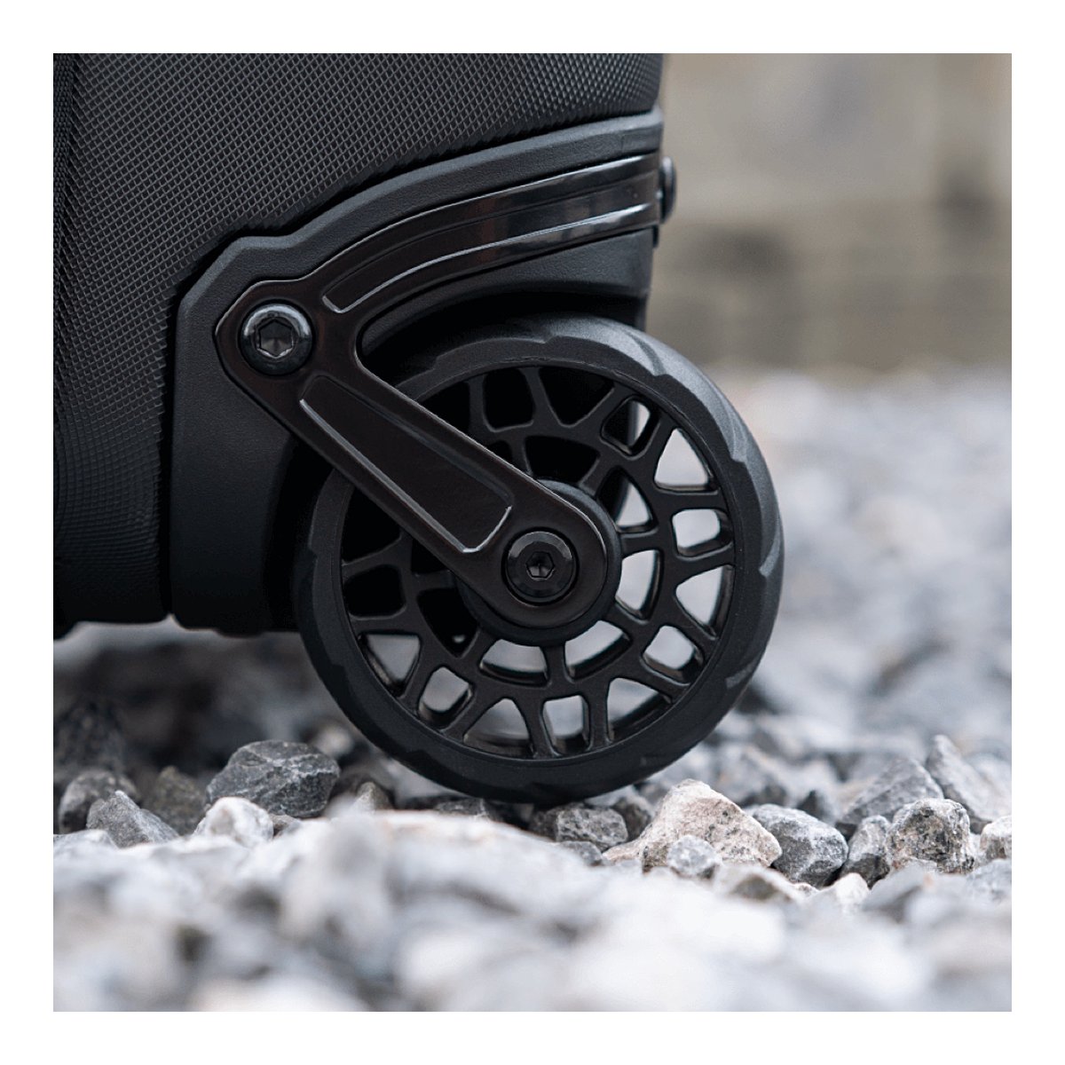 WANDRD Transit Carry-On Roller - Detailansicht der schwarzen Rolle des Produkts auf Kies
