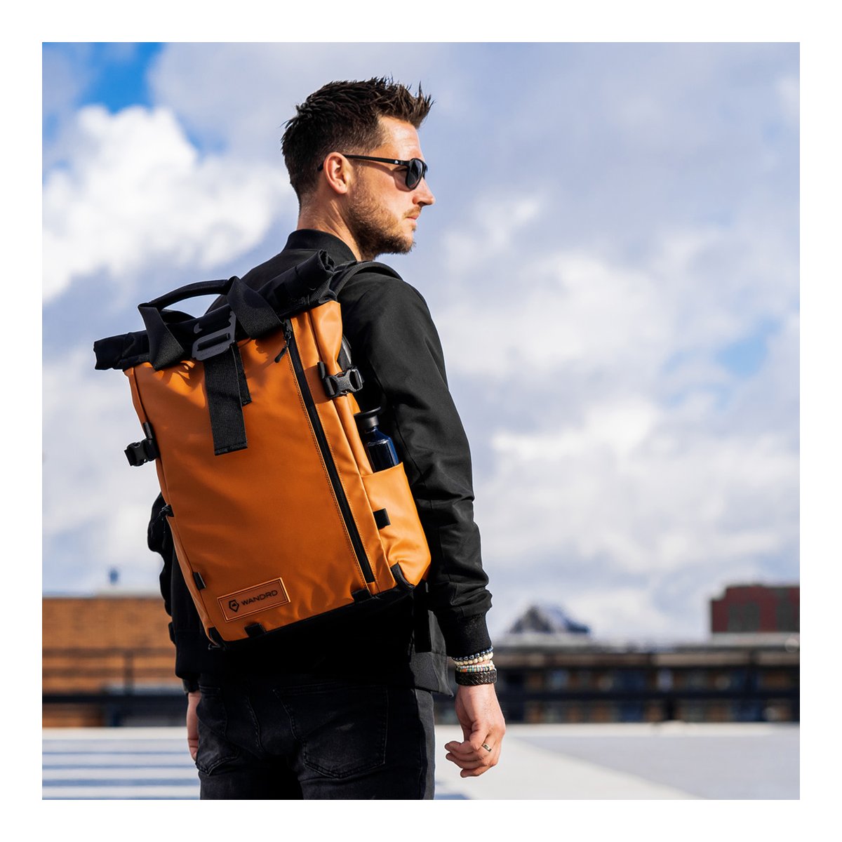 WANDRD PRVKE 21-Liter Sedona Orange Photo Bundle V3 - Anwendungsbeispiel am Mann, Rückansicht des orangefarbenen Rucksacks mit Trinkflasche im Seitenfach.