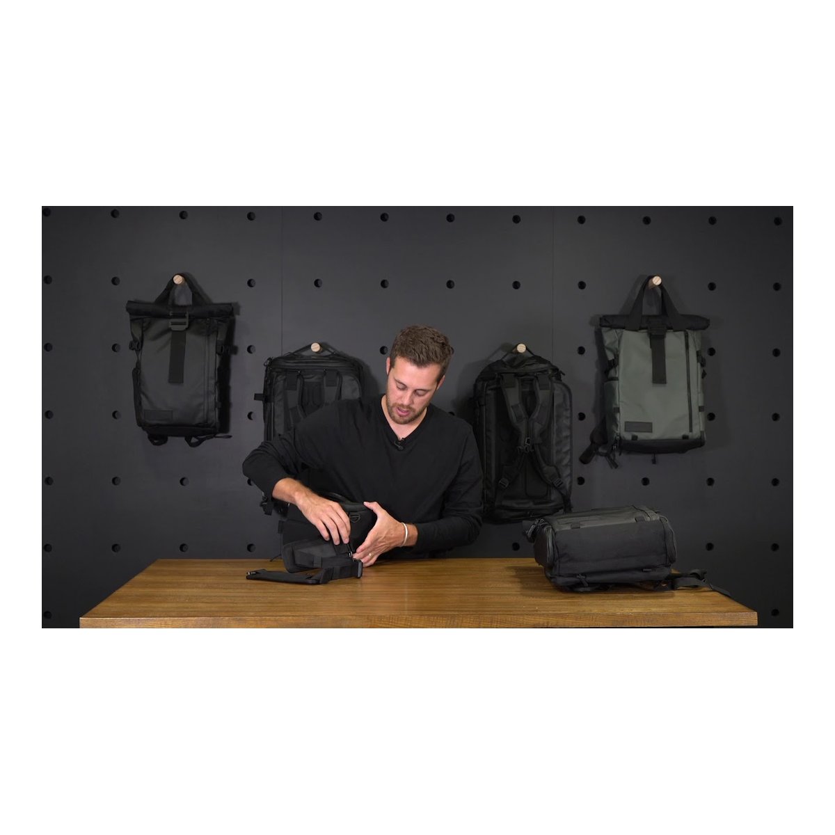 WANDRD Camera Cube Mini+ (31 Liter PRVKE) - Anwendungsbeispiel: Mann öffnet schwarze Tasche auf Holztisch