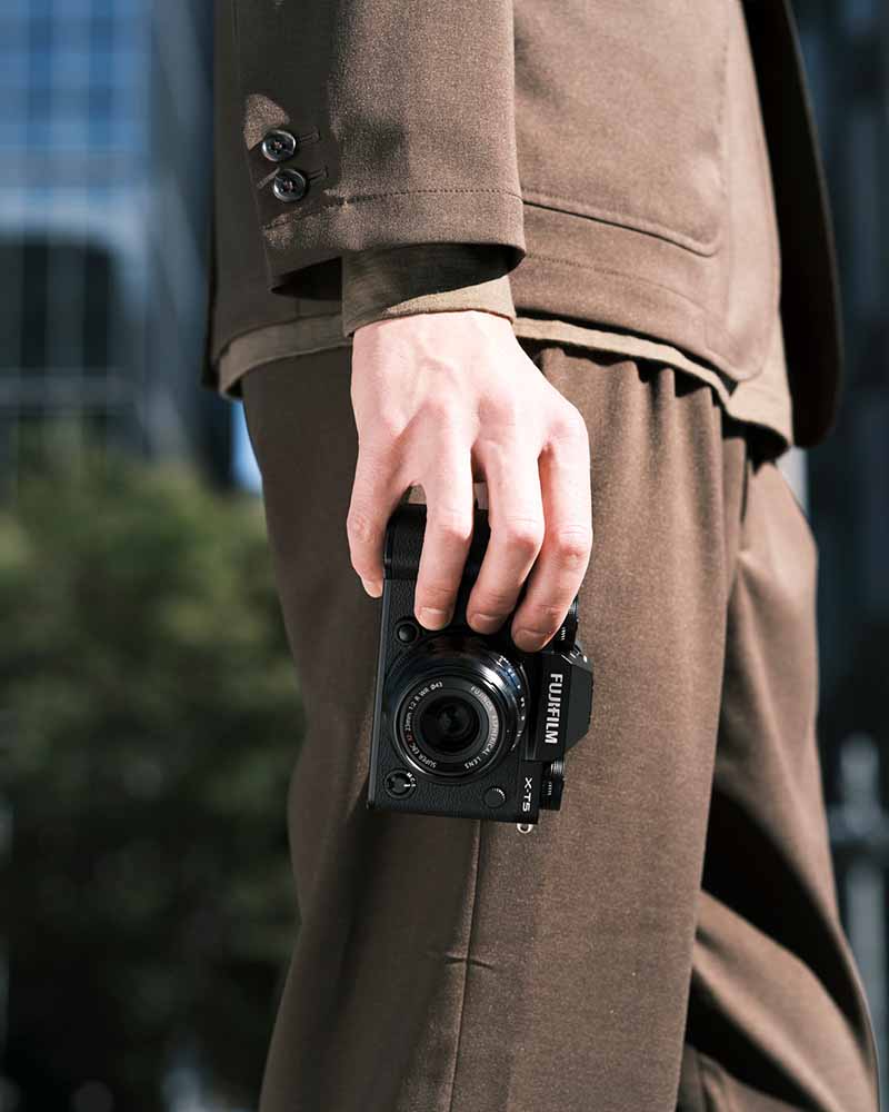 Fujifilm X-T5 in der Hand eines Fotografen, stilvolle Szene in urbaner Umgebung. Ideal für Porträts und Reisen, kompakte Systemkamera für anspruchsvolle Fotografen.