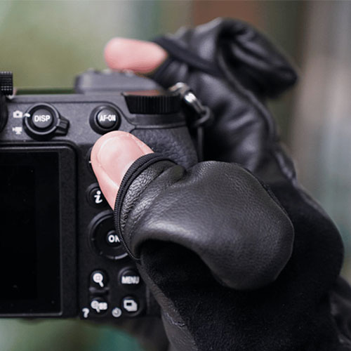 Detailaufnahme einer Hand mit Winter-Fotohandschuh, die die Bedienelemente einer Kamera nutzt, während der Finger freigelegt ist.