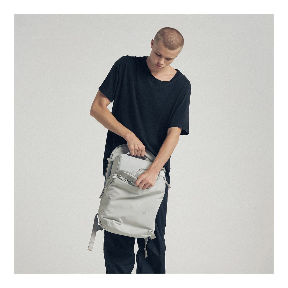 Urth Norite Camera Insert (Aschgrau) - Anwendungsbeispiel: Mann verstaut Laptop in hellgrauem Rucksack.