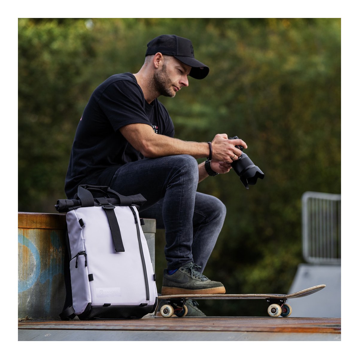 WANDRD PRVKE Lite 11-Liter Uyuni Purple - Anwendungsbeispiel: Heller Roll-Top Rucksack neben sitzendem Mann mit Kamera und Skateboard.