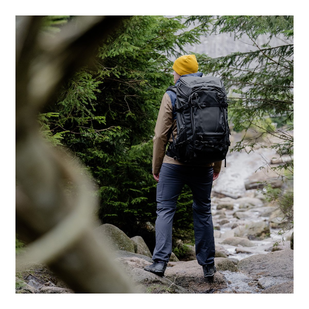 F-Stop DuraDiamond Shinn Essentials Bundle - Anthrazit - Anwendungsbeispiel: Rückansicht einer Person mit schwarzem Wanderrucksack auf Felsen im Wald.