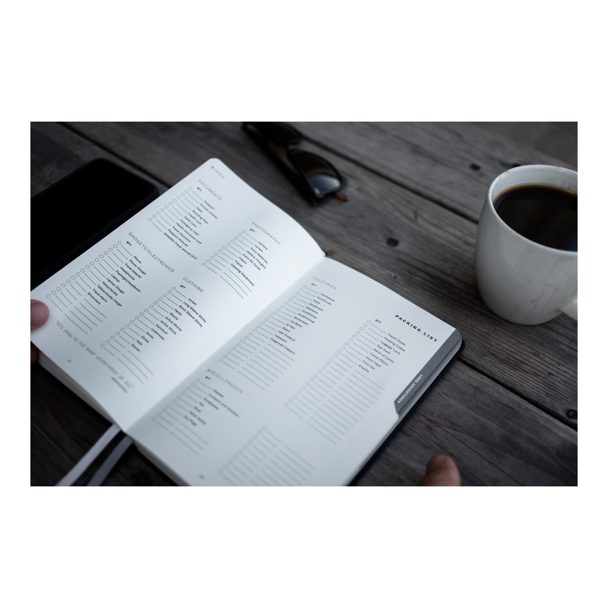 WANDRD THE TRAVEL JOURNAL Yellow - Innenansicht: Packliste des Notizbuchs auf einem Holztisch mit Kaffee und Sonnenbrille WANDRD THE TRAVEL JOURNAL Yellow - Innenansicht: Packliste des Notizbuchs auf einem Holztisch mit Kaffee und Sonnenbrille