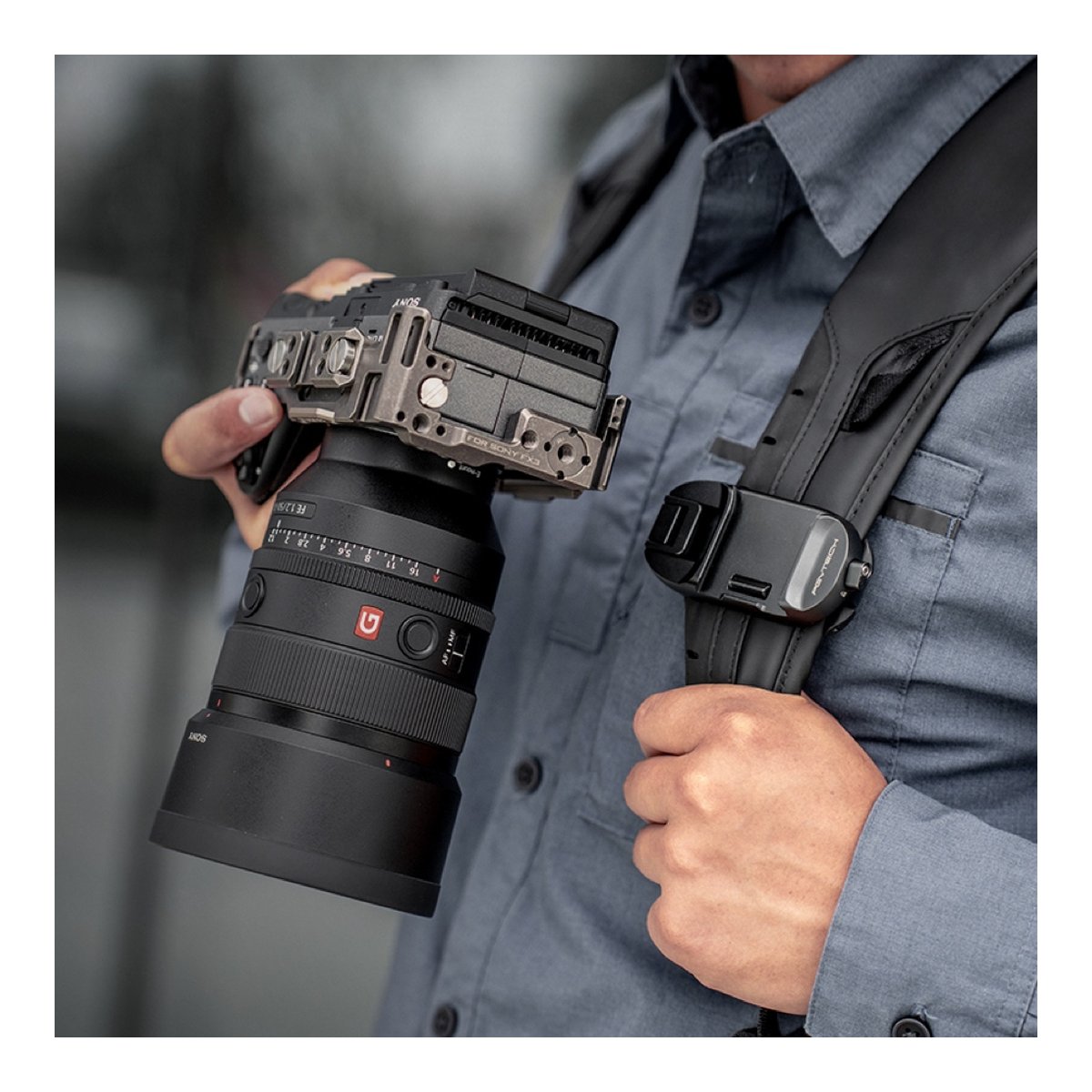 PGYTECH Beetle Camera Clip - Anwendungsbeispiel: Person hält Kamera mit Käfig und Objektiv, Schultergurt mit Schnellverschluss-System.