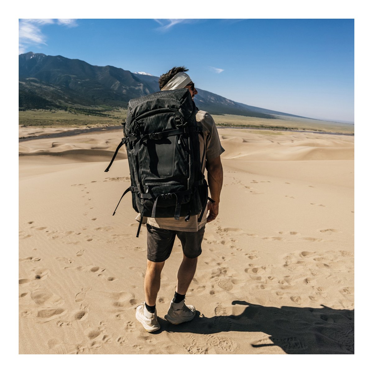 F-Stop DuraDiamond Shinn - Anthrazit - Anwendungsbeispiel: Rückansicht eines Mannes mit großem schwarzen Rucksack in einer Dünenlandschaft. F-Stop DuraDiamond Shinn - Anthrazit - Anwendungsbeispiel: Rückansicht eines Mannes mit großem schwarzen Rucksack in einer Dünenlandschaft.