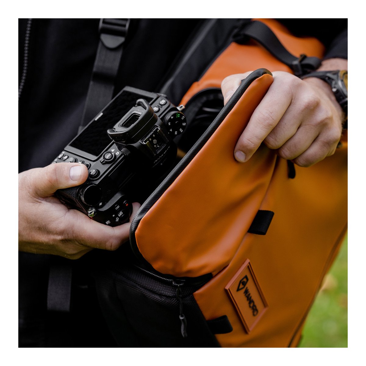 WANDRD PRVKE 21-Liter Sedona Orange Photo Bundle V3 - Anwendungsbeispiel: Hände verstauen Kamera in orangem Fotorucksack