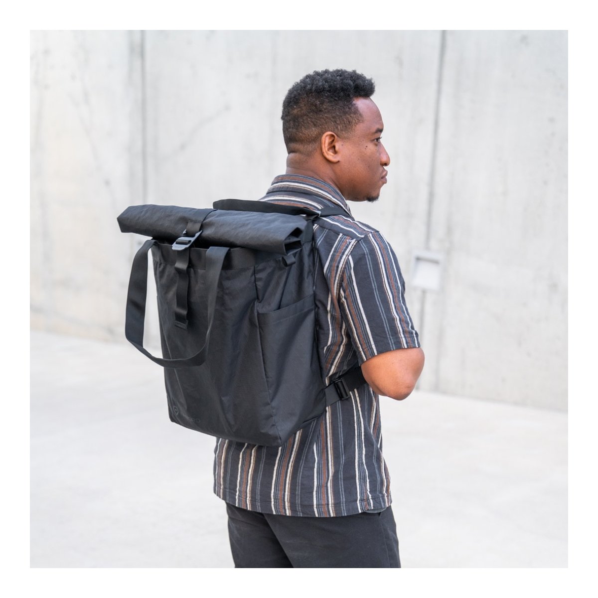 WANDRD Tote Backpack - Anwendungsbeispiel: Schwarzer Roll-Top-Rucksack auf dem Rücken. WANDRD Tote Backpack - Anwendungsbeispiel: Schwarzer Roll-Top-Rucksack auf dem Rücken.