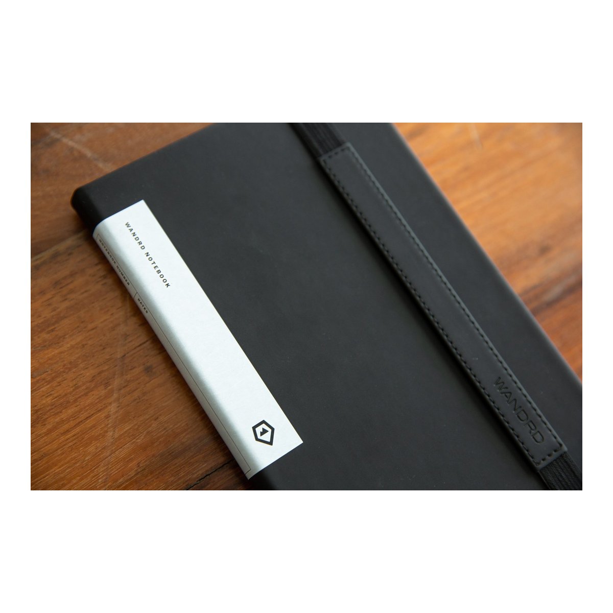 WANDRD NOTEBOOK Yellow - Detailansicht: Schwarzes Wandrd Notizbuch mit weißem Seitenband und Gummiband mit WANDRD-Logo.
