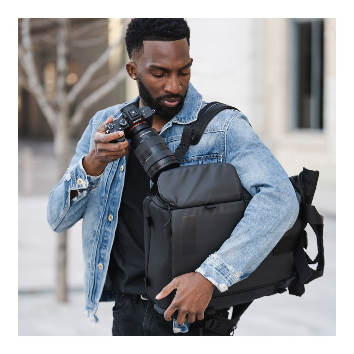 WANDRD PRVKE Lite 11-Liter Black - Anwendungsbeispiel: Mann verstaut Kamera in schwarzem Fotorucksack