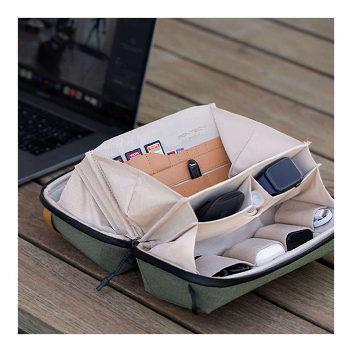 PGYTECH Tech Pouch(Moss Green) - Anwendungsbeispiel: Geöffnete Organizer-Tasche mit Fächern voller Tech-Zubehör, auf Holztisch neben Laptop.