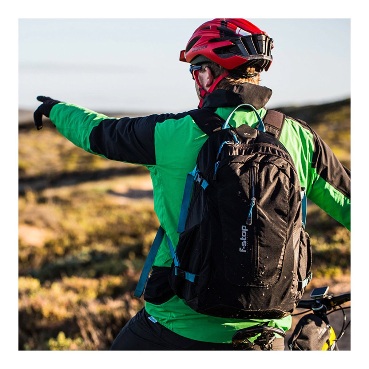 F-Stop Guru UL Essentials Bundle - Anwendungsbeispiel: Radfahrer mit schwarzem Rucksack und rotem Helm von hinten, zeigt in die Ferne.
