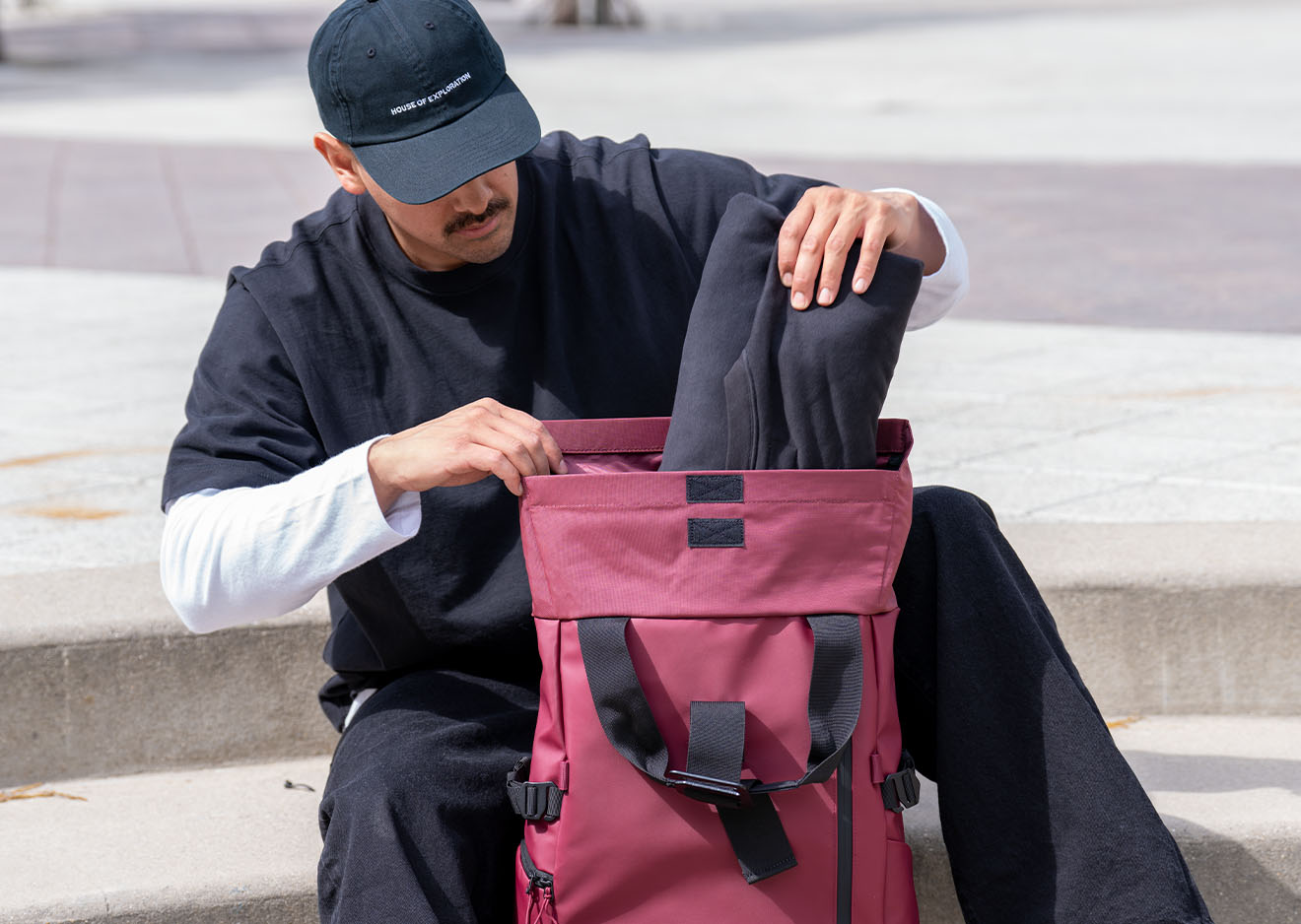 Mann packt Kleidung in einen roten Wandrd PRVKE Rucksack im urbanen Umfeld