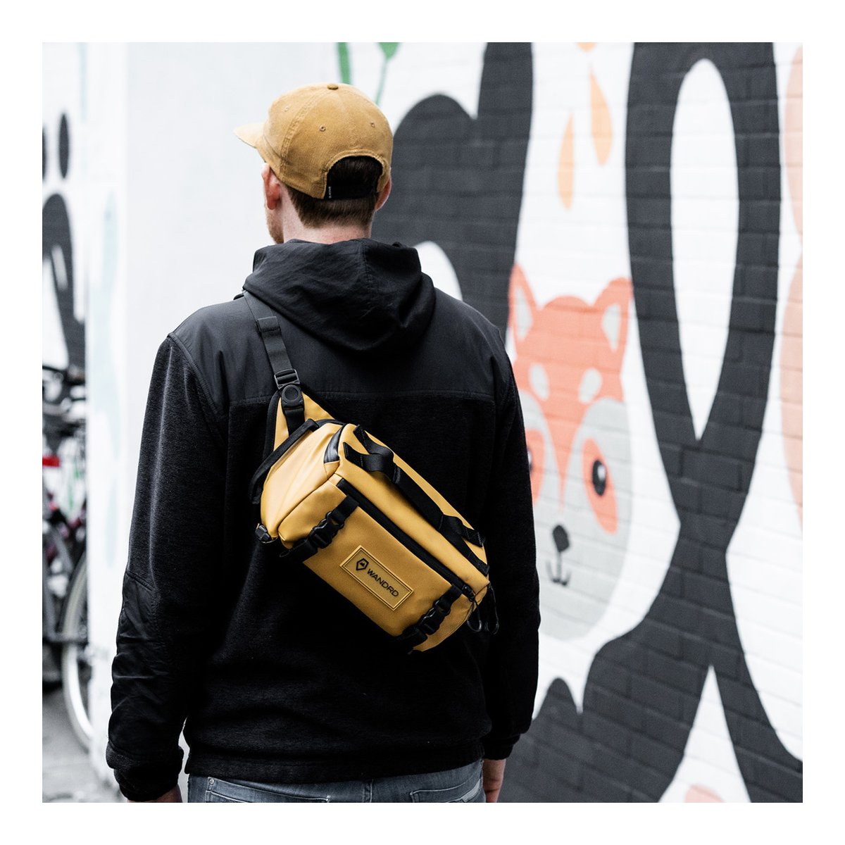 WANDRD ROGUE Sling 6L Dallol Yellow - Anwendungsbeispiel: Gelbe Hüfttasche von hinten schräg über dem Oberkörper einer Person getragen.