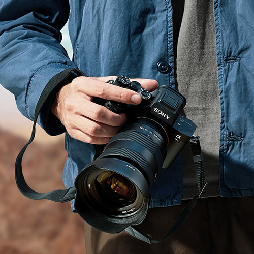 Person hält eine Sony Vollformatkamera mit Zoomobjektiv bei einer Outdoor-Aufnahme in der Hand